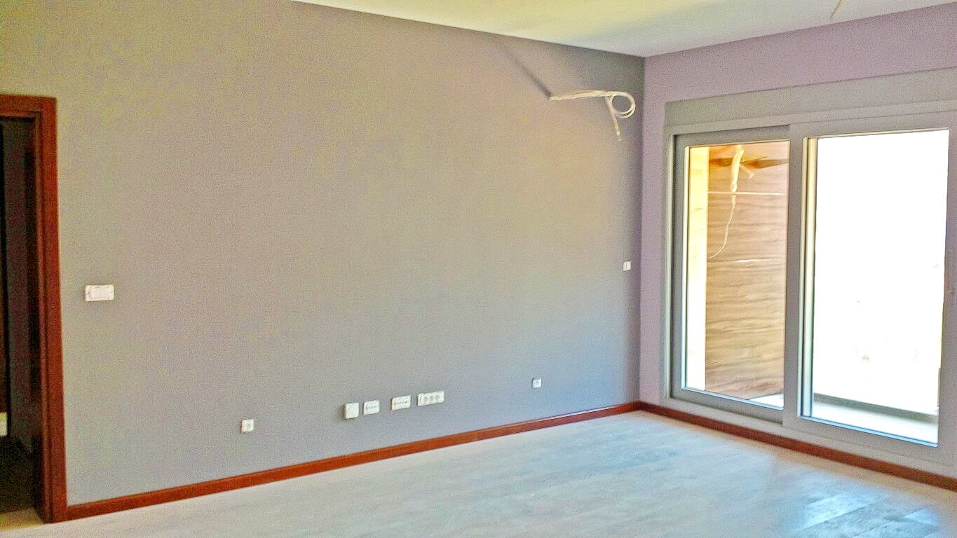 Helles Wohnzimmer in einer Wohnung in Kotor, Montenegro: graue Wände, Panoramafenster und Zugang zur Terrasse, moderne Renovierung.