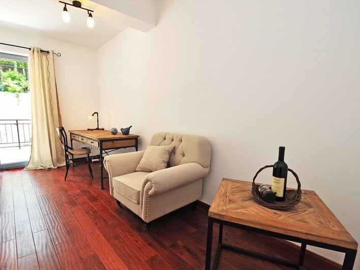 Gemütliches Wohnzimmer in einer Wohnung in Risan, Montenegro: Sessel, hölzerner Schreibtisch, Parkettboden und Zugang zum Balkon.