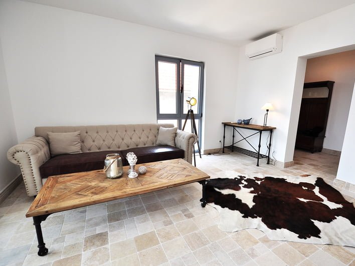 Wohnzimmer in einer Wohnung in Risan, Montenegro: beige Couch, hölzerner Couchtisch und Steinboden.