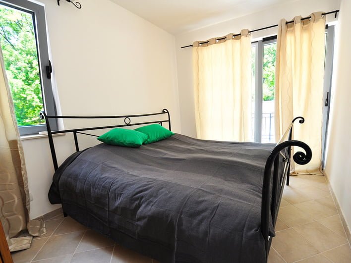 Helles Schlafzimmer mit schmiedeeisernem Bett und Zugang zum Balkon in einer Wohnung, Stadt Risan, Montenegro.