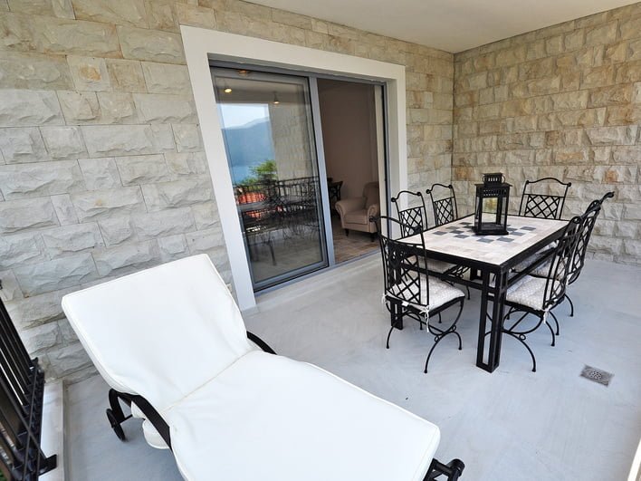 Terrasse mit Schmiedemöbeln und Meerblick in einer Wohnung in Risan, Montenegro: Steinverkleidung der Wände und eine Sonnenliege.