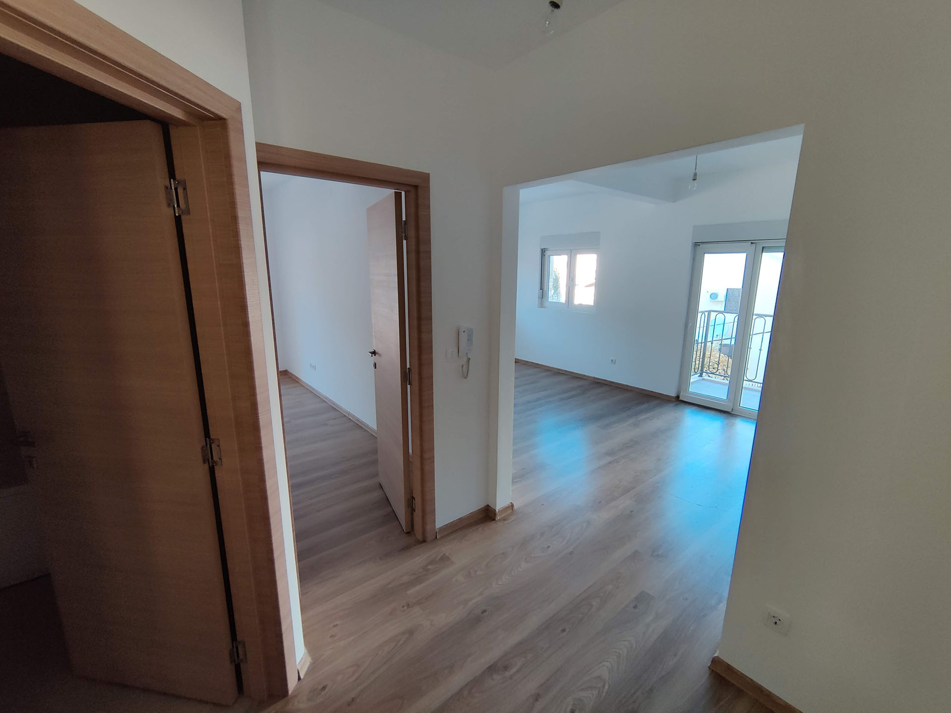 Bright living room with laminate flooring in an apartment in Bečići, Montenegro: view of the rooms, interior doors, and access to the balcony.