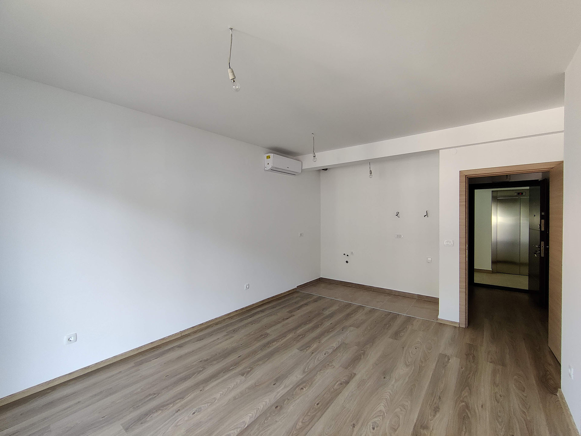 Bright living room with laminate flooring and air conditioning in a new apartment in Bečići, Montenegro, view of the entrance door and elevator.