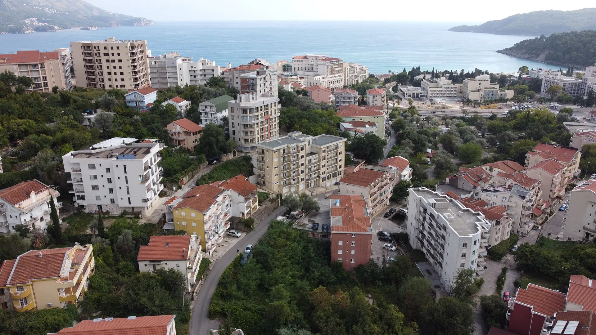 Панорамный вид на жилой район и море в Бечичи, Черногория: современные многоквартирные дома среди зелени.