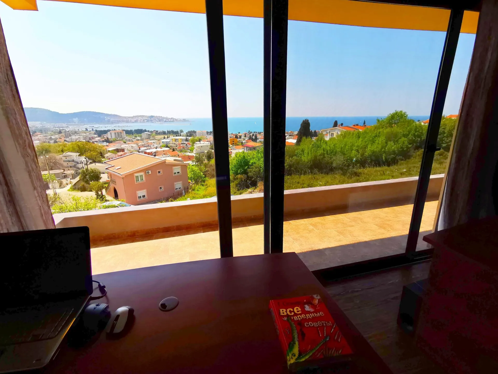 Meer- und Stadtblick auf Bar vom Wohnzimmer der Villa in Montenegro: Panoramafenster, Terrasse und Arbeitsplatz mit Laptop.