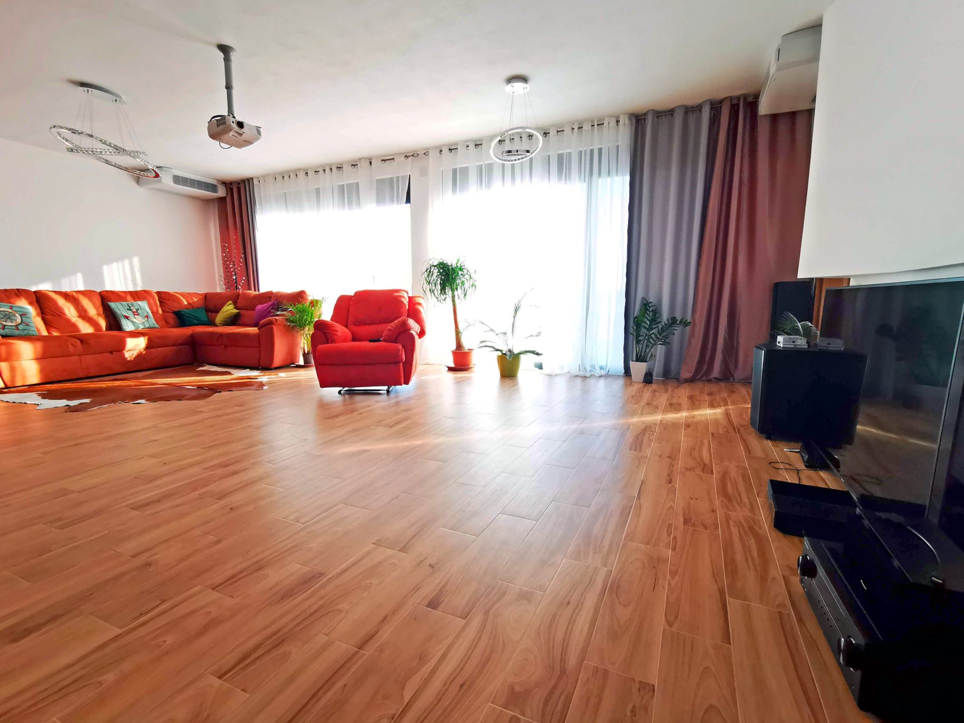 Przestronny salon z czerwoną sofą i projektorem w willi w mieście Bar, Czarnogóra. Jasne wnętrze z panoramicznymi oknami.