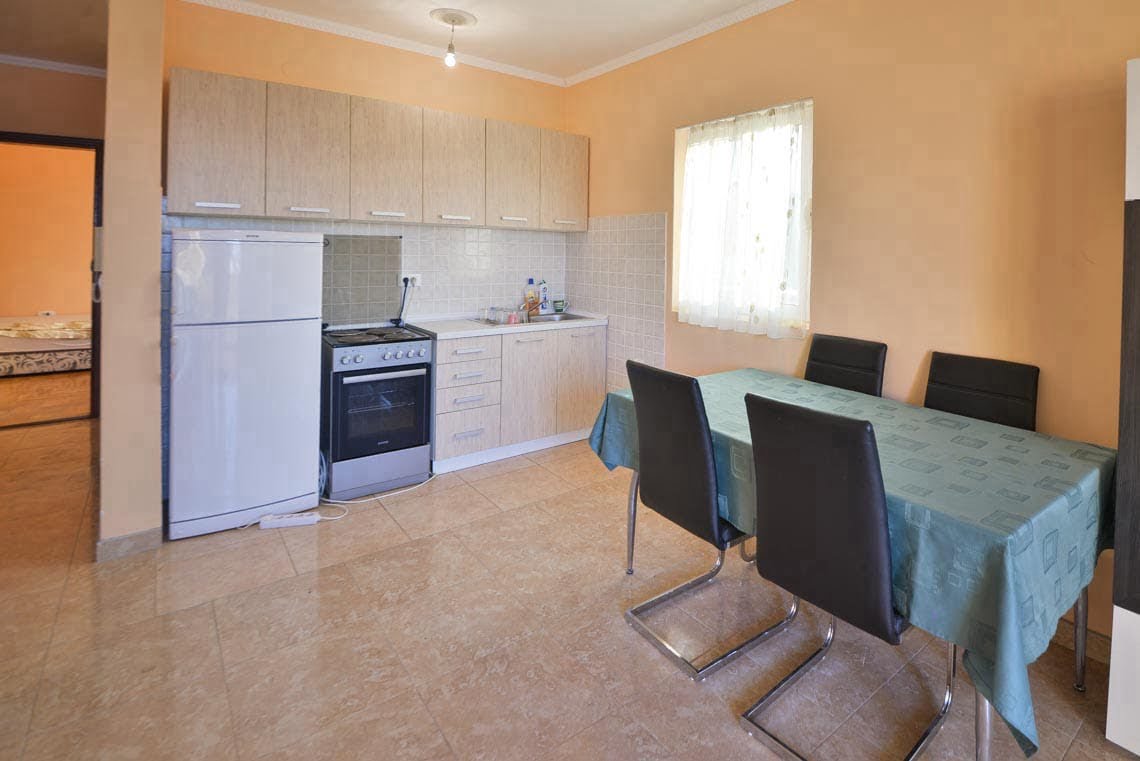 Kitchen with dining area in an apartment in Utjeha, Montenegro: light-colored cabinets, stove, refrigerator, and a table with chairs.