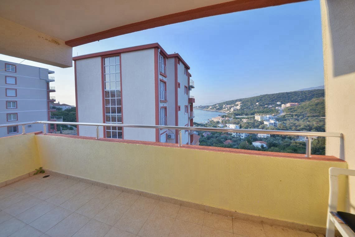 View from the apartment balcony in Utjeha, Montenegro: a panorama of the sea, mountains, and neighboring houses, tiled floor, railing.