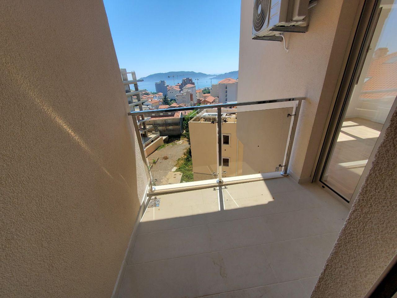 Moderan balkon sa staklenom ogradom, popločanim podom i pogledom na grad i more.