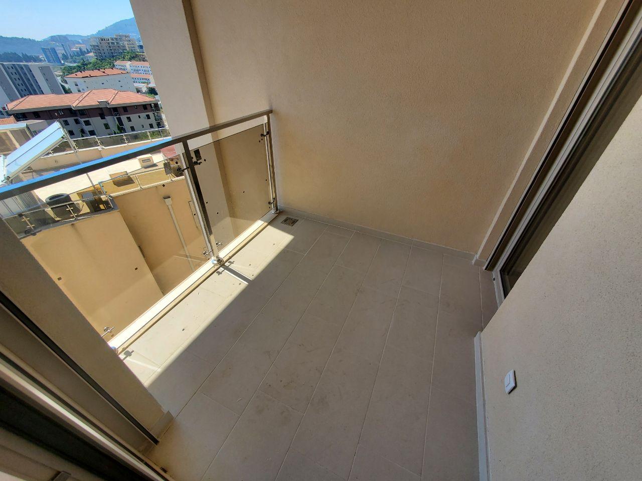 Usak balkon sa staklenom ogradom, popločanim podom i pogledom na grad.