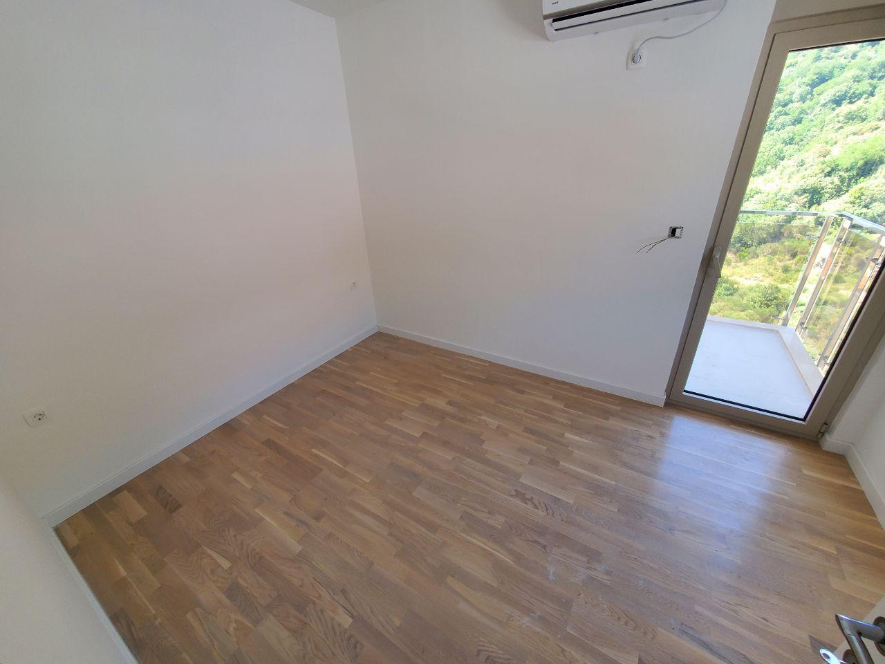 Prazna nameštena spavaća soba sa drvenim podom i balkonskim vratima.