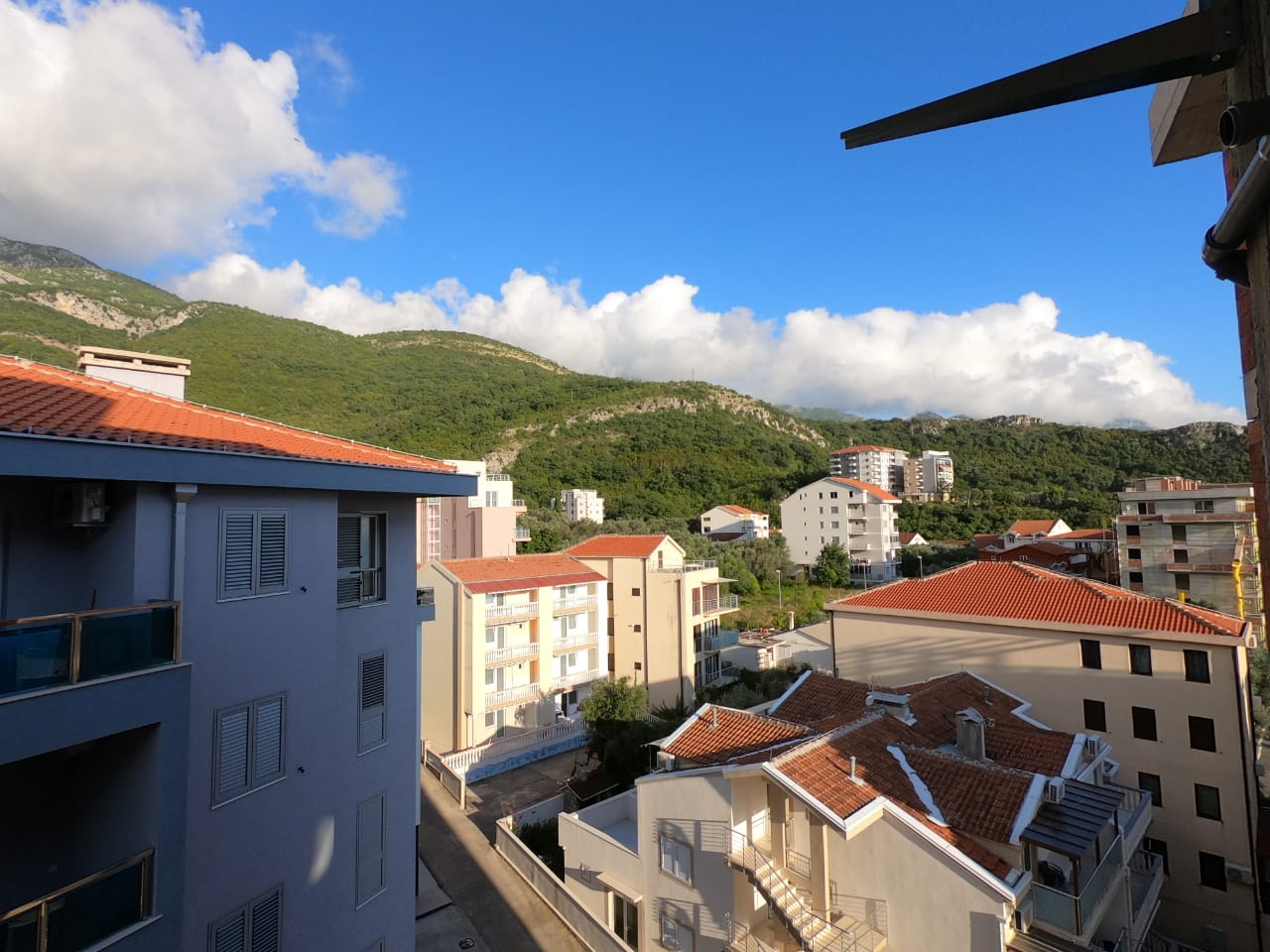 Pogled sa balkona na grad, planine i oblačno nebo.
