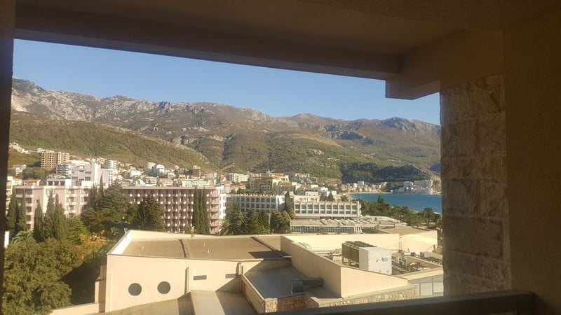 Karadağ, Bečići’deki dairenin balkonundan görünüm: güneşli bir günde dağlar, oteller ve Adriyatik Denizi panoraması.