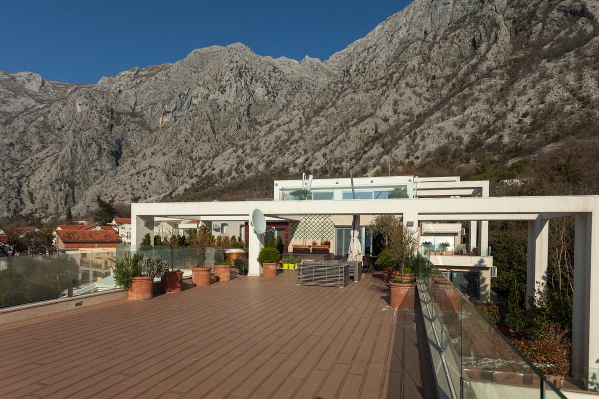 Spacieuse terrasse avec mobilier et vue sur les montagnes dans un appartement, Ljuta, Monténégro. Finitions modernes et garde-corps en verre.