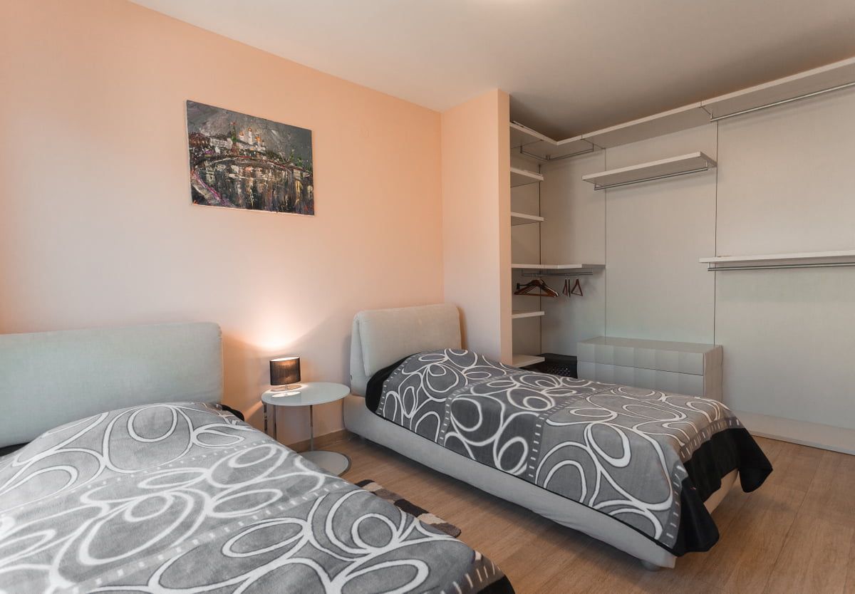 Chambre avec deux lits et placard intégré dans un appartement à Ljuta, Monténégro. Intérieur lumineux avec un tableau au mur.