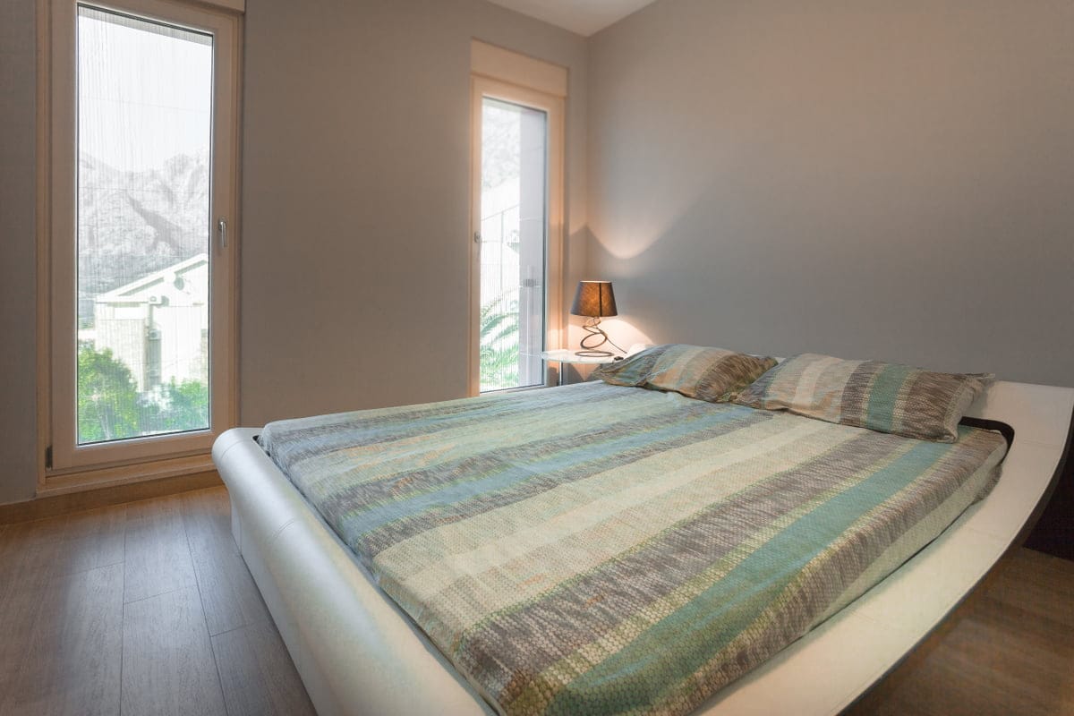 Chambre moderne avec lit double dans un appartement à Ljuta, Monténégro, avec des fenêtres panoramiques et vue sur les montagnes.