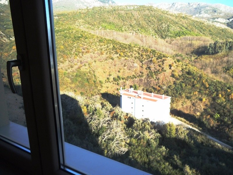 Blick aus dem Fenster einer Wohnung in Bečići, Montenegro: Panorama auf grüne Berge und ein benachbartes Wohngebäude mit rotem Dach.