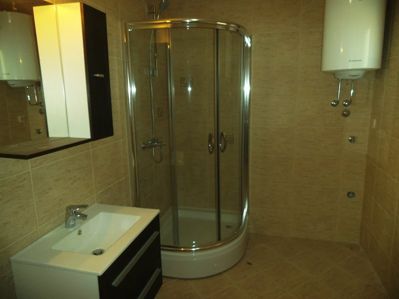 Badezimmer in einer Wohnung in Bečići, Montenegro: Duschkabine, Waschtischunterschrank mit Waschbecken und Boiler, mit beigen Fliesen ausgestattet.