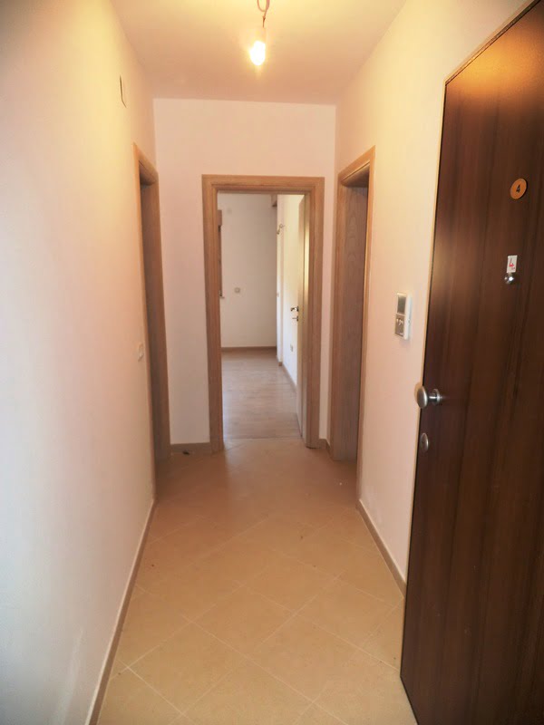 Heller Flur in einer Wohnung in Bečići, Montenegro: Fliesenboden, Innentüren aus hellem Holz und Eingangstür.