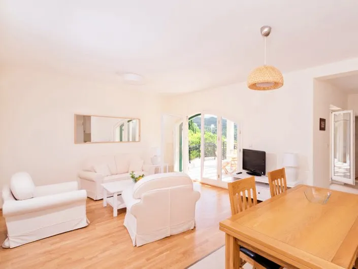 Helles Wohnzimmer mit weißen Möbeln und Essbereich in einer Wohnung in Herceg Novi, Montenegro, mit Zugang zur Terrasse.