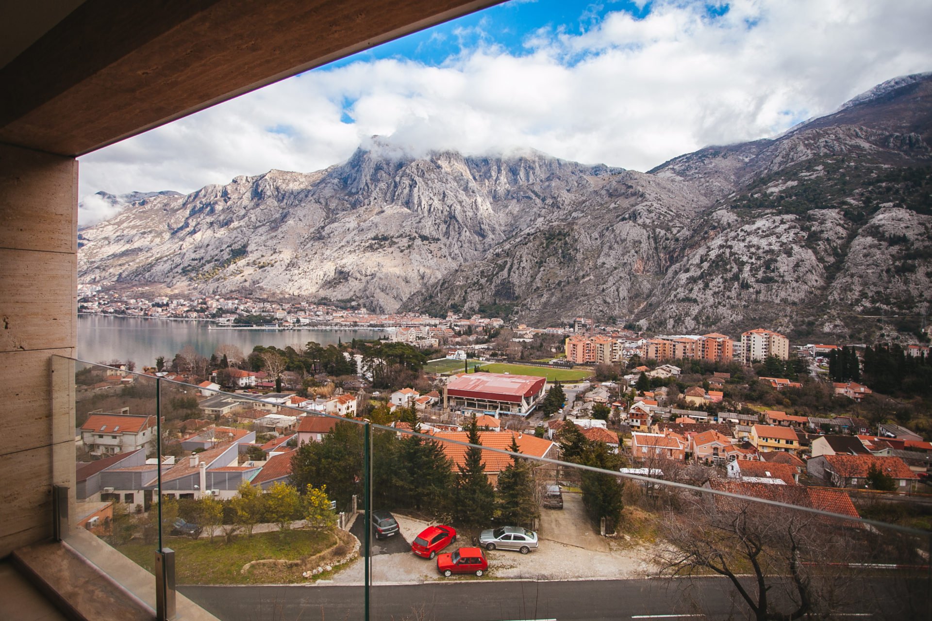 View from the balcony of a residential complex in Kotor, Montenegro: a panorama of mountains, the bay, and the city with modern glass finishing.