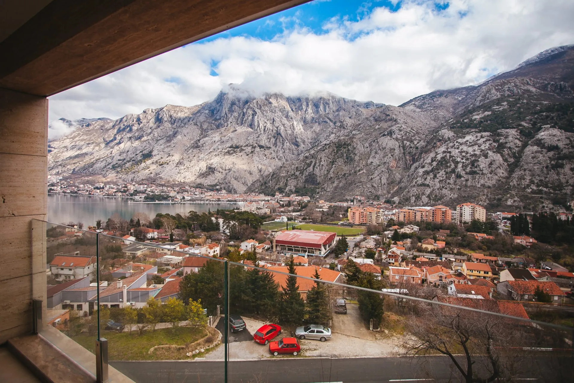 Blick vom Balkon eines Wohnkomplexes in Kotor, Montenegro: Panorama von Bergen, Bucht und Stadt mit moderner Glasfassade.