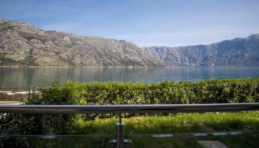 Stoliv’deki dairenin balkonundan manzara, Boka Kotorska Körfezi, Karadağ: yeşil bitki örtüsü arasından deniz ve dağların panoraması.