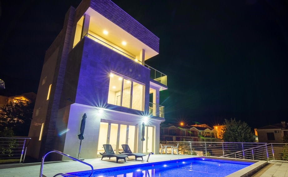 Moderne dreistöckige Villa mit Pool und nächtlicher Beleuchtung in Bečići, Montenegro. Fassadenansicht mit Terrasse.