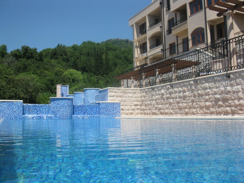Offener Pool mit Kaskade am Wohnkomplex in Igalo, Herceg Novi, Montenegro, vor dem Hintergrund von Bergen und Grün.