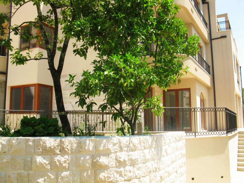 Fassade des Wohnkomplexes in Igalo, Montenegro: Steinverkleidung, Terrassen mit schmiedeeisernen Geländern und ein grüner Baum im Innenhof.