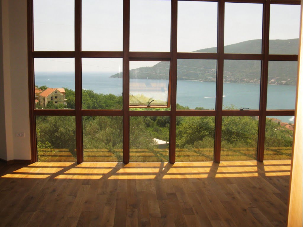 Panoramafenster im Wohnzimmer mit Blick auf das Meer und die Berge, Igalo, Montenegro. Heller Raum mit Holzboden.