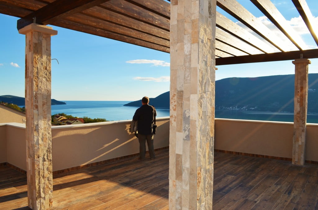 Geräumige Terrasse mit Meerblick in einer Wohnanlage in Igalo, Montenegro: Steinsäulen und Holzbelag.