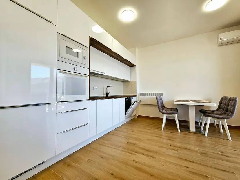Moderne weiße Küche mit Geräten und Essbereich in einer Wohnung in Budva, Montenegro. Helles Interieur mit Laminatboden.