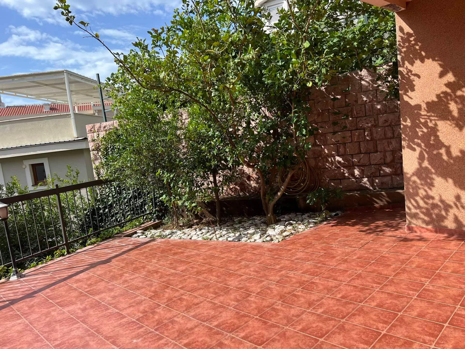 Terrasse confortable avec carrelage et arbre verdoyant dans un duplex, Petrovac, Monténégro. Vue sur une cour privée avec mur en pierre.
