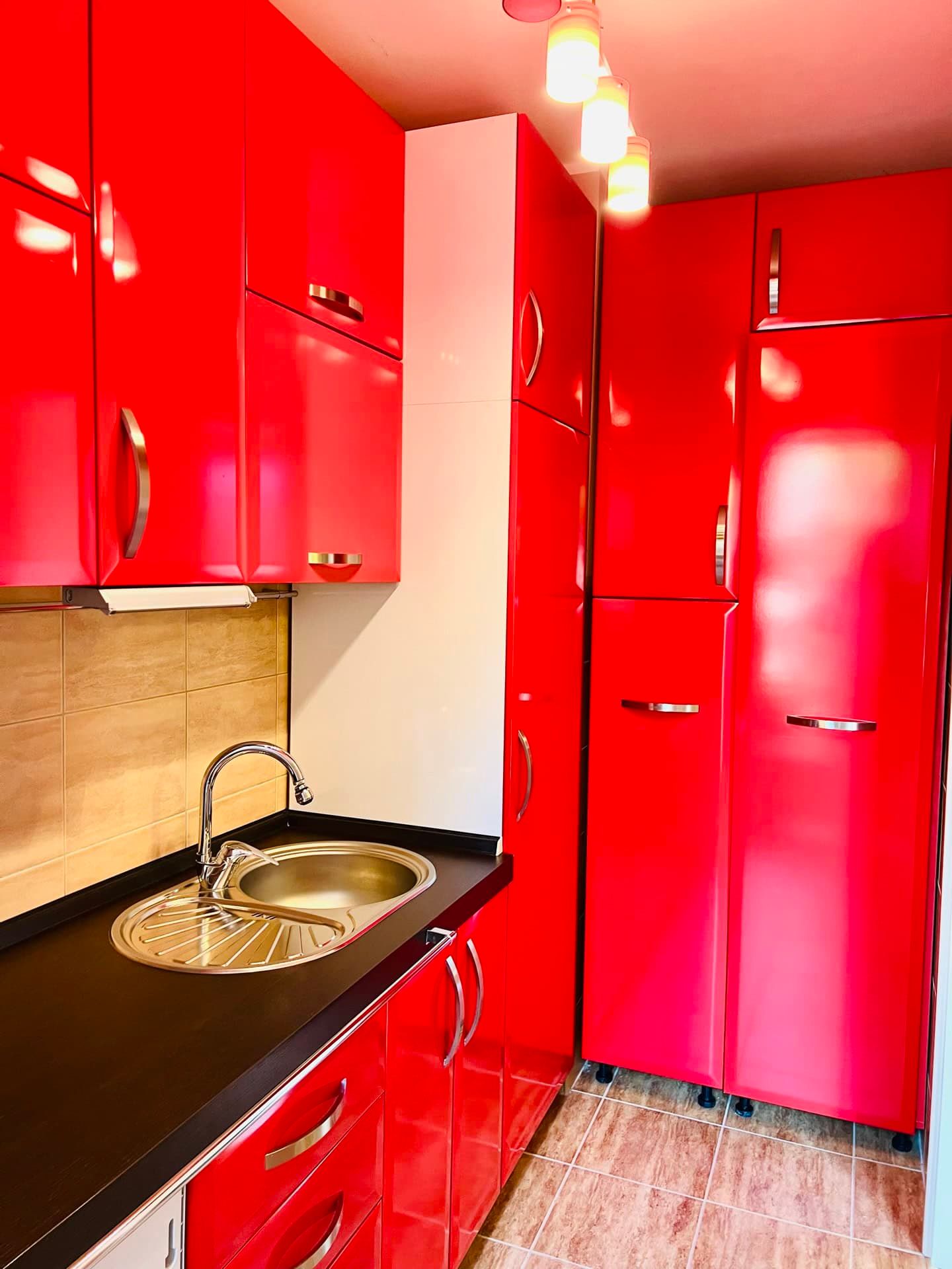 Cuisine lumineuse avec façades rouges brillantes dans l’appartement, Petrovac, Monténégro : plan de travail noir et électroménager intégré.