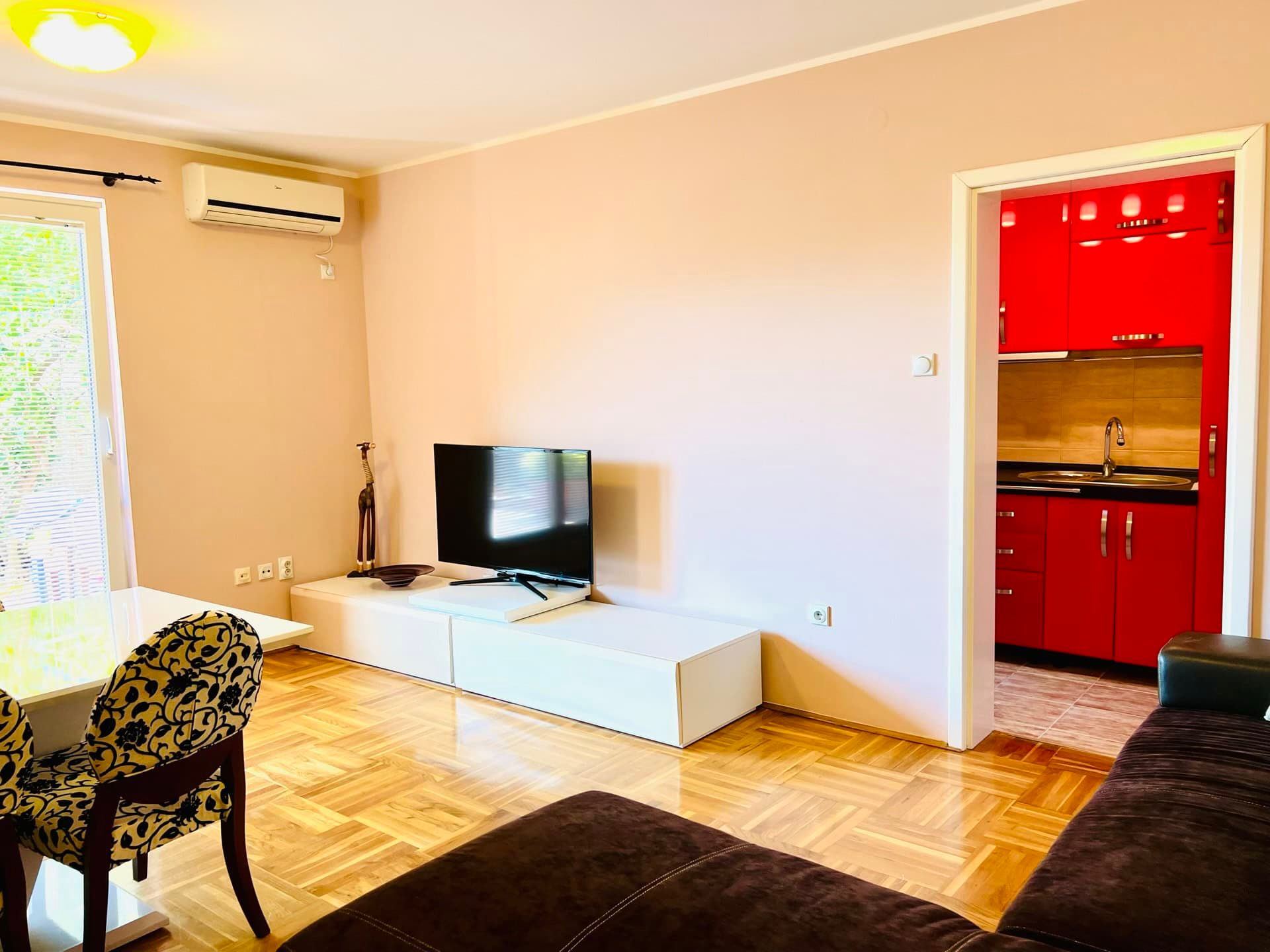 Salon avec parquet, coin TV et cuisine rouge éclatante dans un appartement à Petrovac, Monténégro.