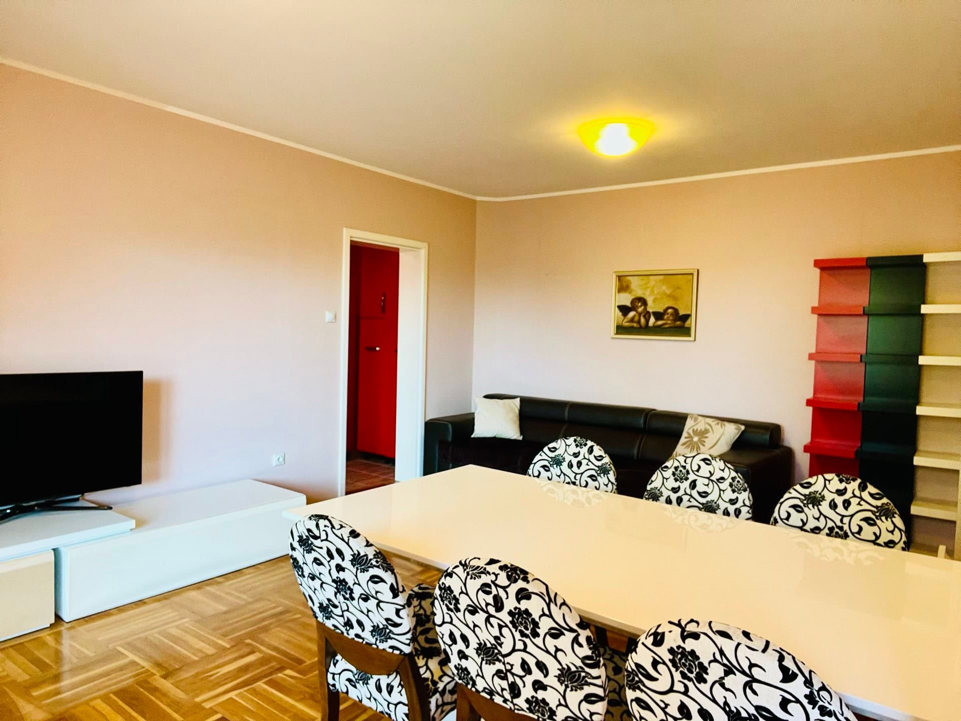 Salon dans un duplex à Petrovac, Monténégro : coin repas avec table blanche, chaises à imprimé floral et espace TV.