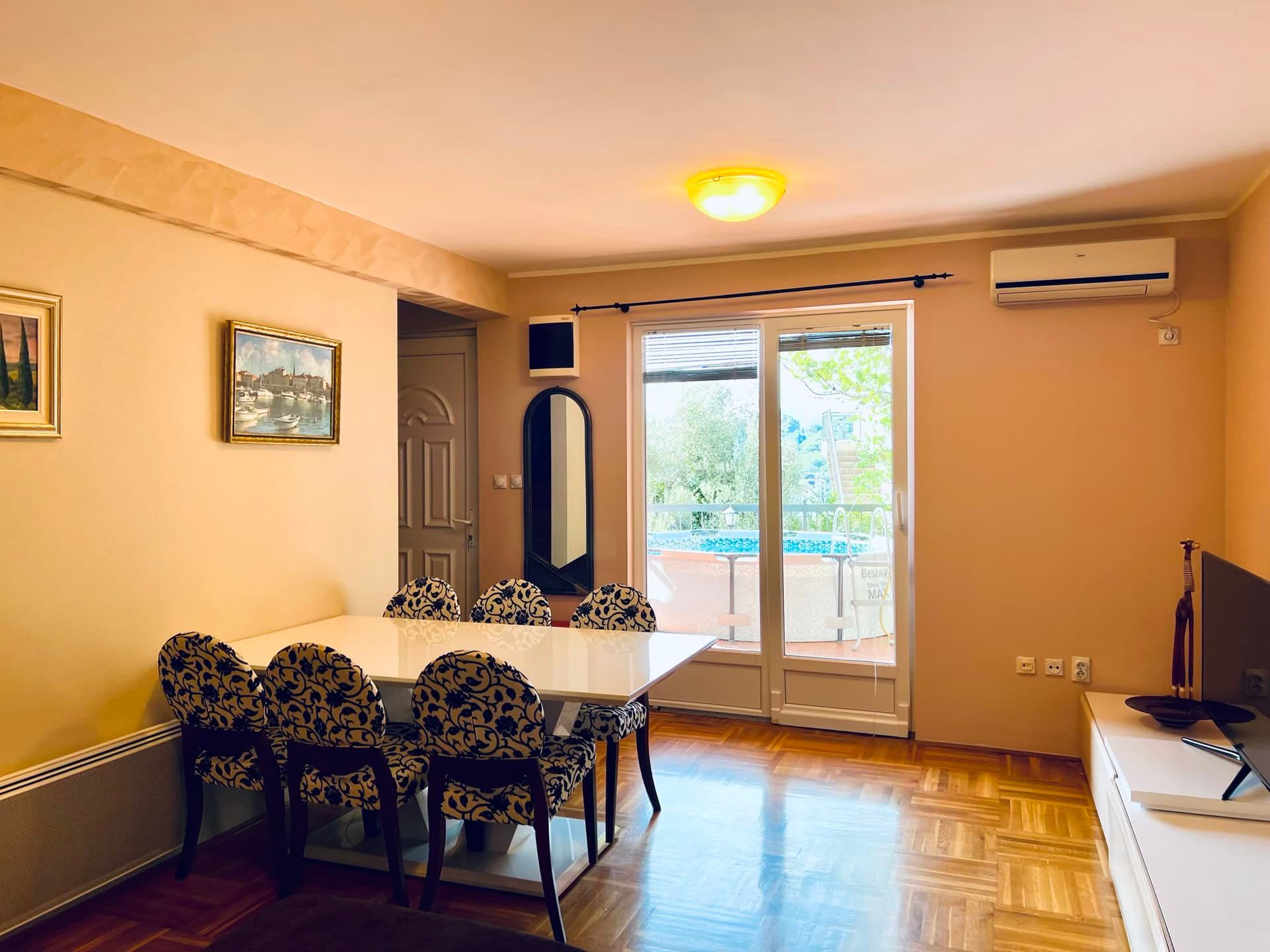 Salon avec coin repas dans un appartement à Petrovac, Monténégro : parquet, accès à la terrasse avec piscine et climatisation.