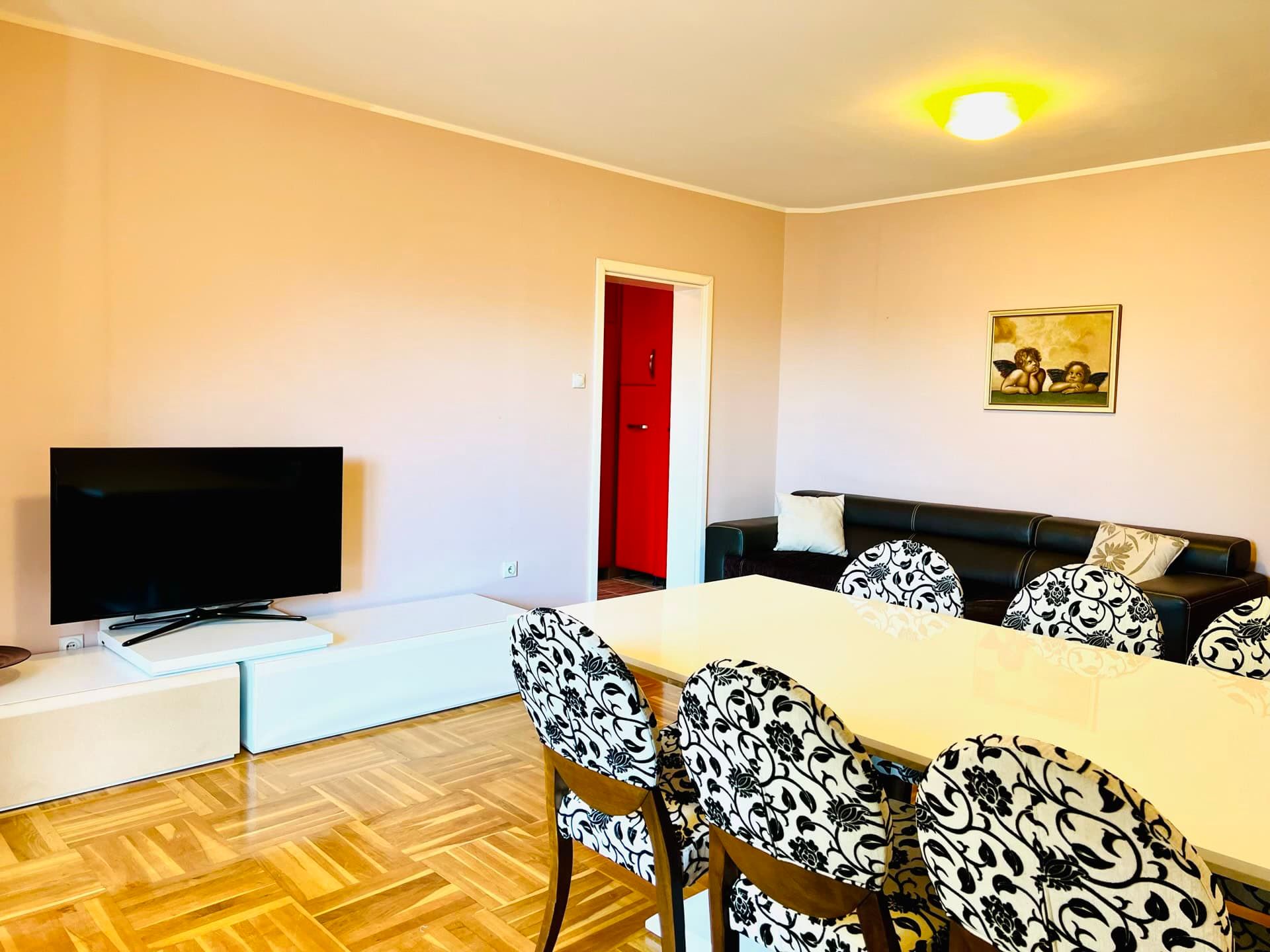 Salon dans un duplex à Petrovac, Monténégro : coin repas avec chaises à motif, espace TV et canapé en cuir noir.