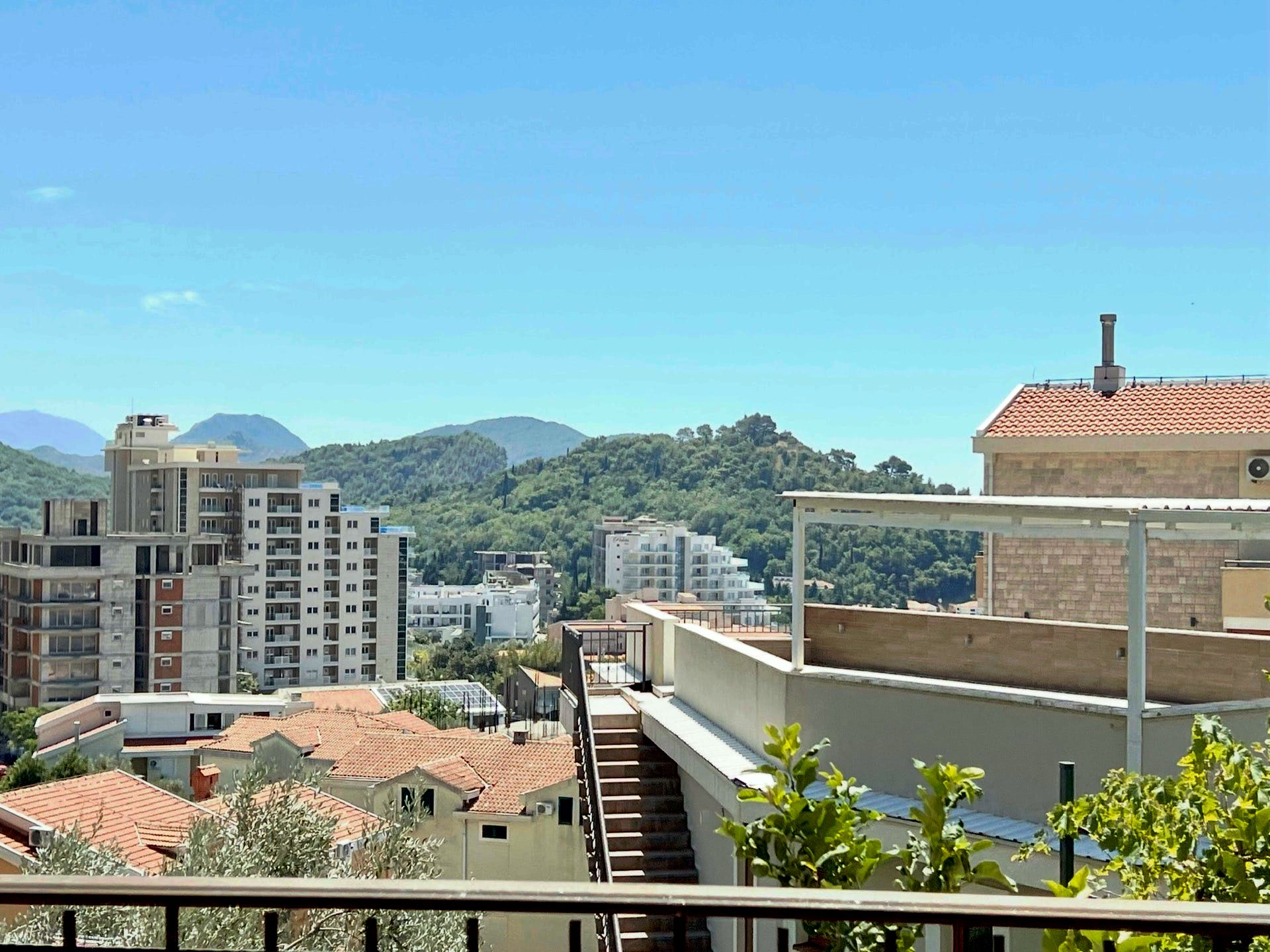 Vue depuis le balcon du duplex à Petrovac, Monténégro : panorama de la ville, toits en tuiles et montagnes verdoyantes à l’horizon.