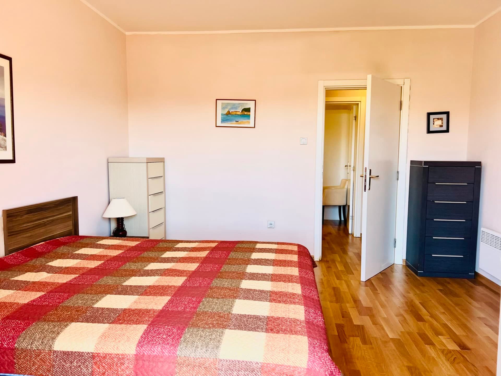Chambre lumineuse avec lit double et parquet dans un appartement à Petrovac, Monténégro. Vue sur l’intérieur avec des commodes.