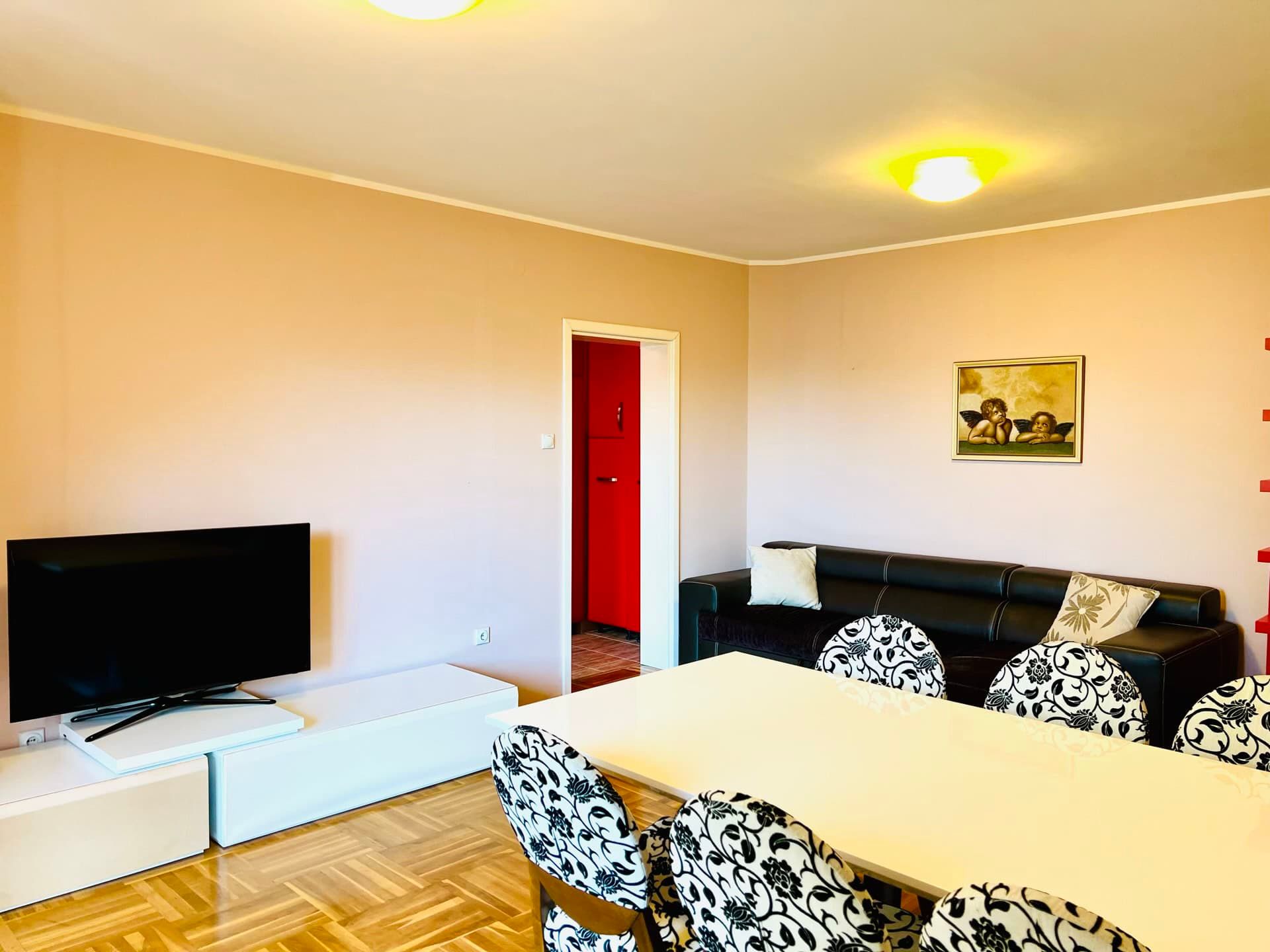 Salon dans un duplex à Petrovac, Monténégro : canapé noir, table à manger avec chaises et coin TV avec parquet.