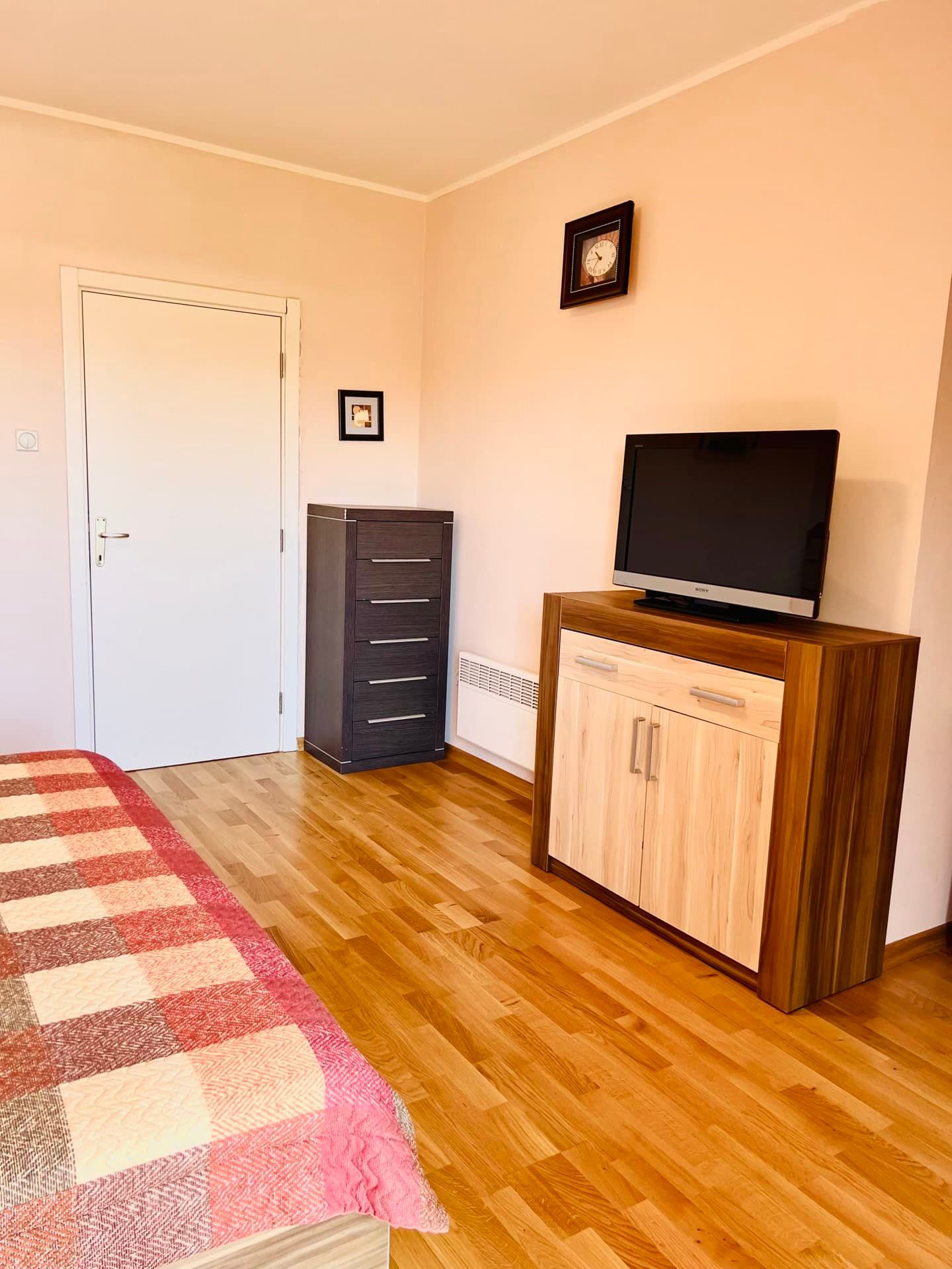 Chambre dans un appartement à Petrovac, Monténégro : parquet, commode, meuble TV et lit avec couvre-lit à carreaux.