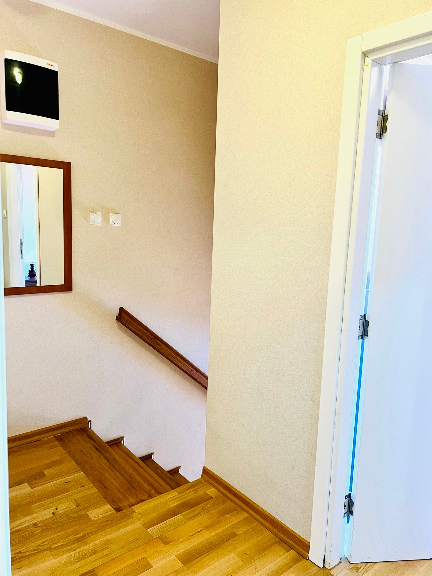 Intérieur lumineux de l’escalier dans un duplex, Petrovac, Monténégro : marches en bois, rampe et miroir mural dans l’entrée.