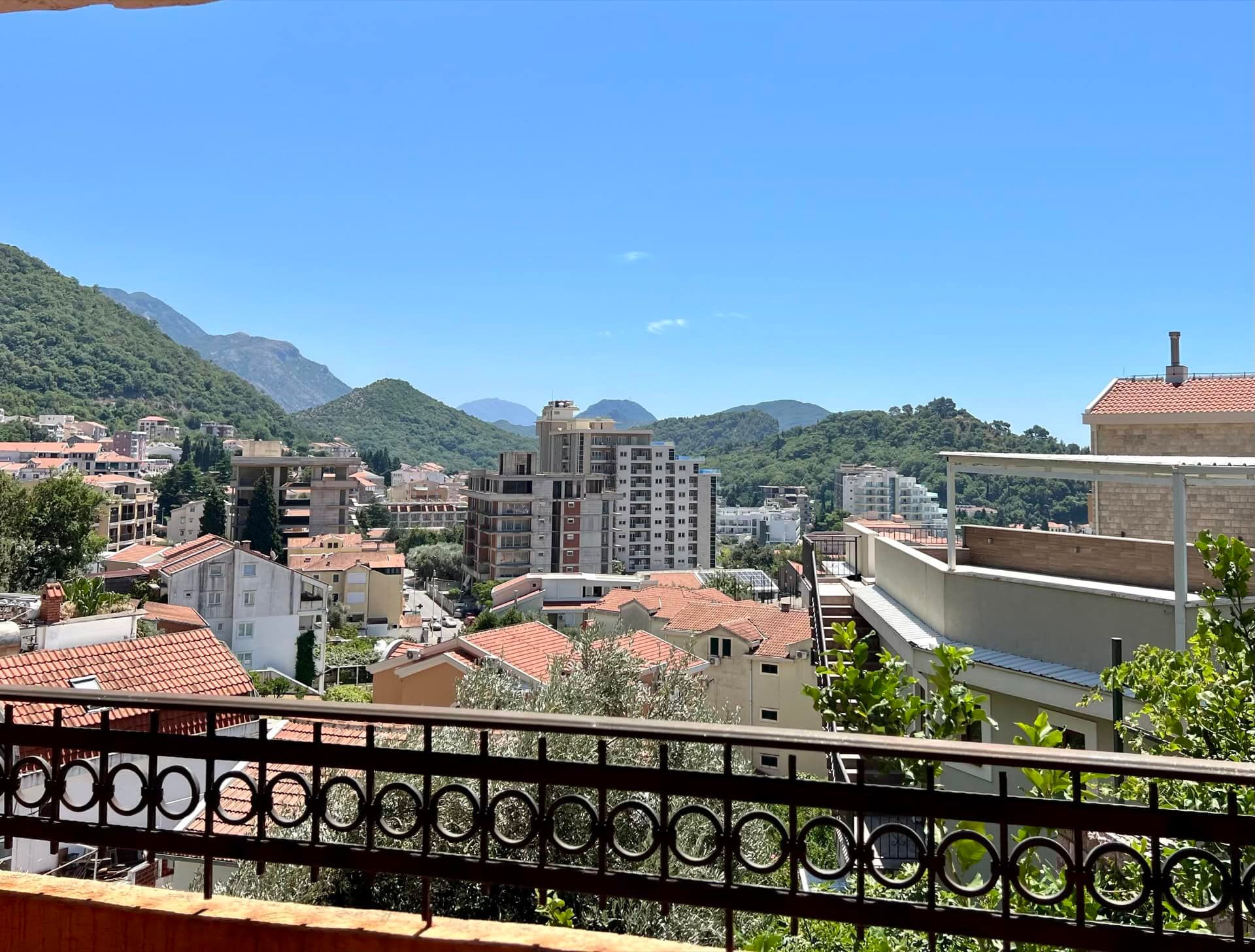 Vue depuis le balcon du duplex à Petrovac, Monténégro : panorama de la ville, toits en tuiles et montagnes verdoyantes à l’horizon.