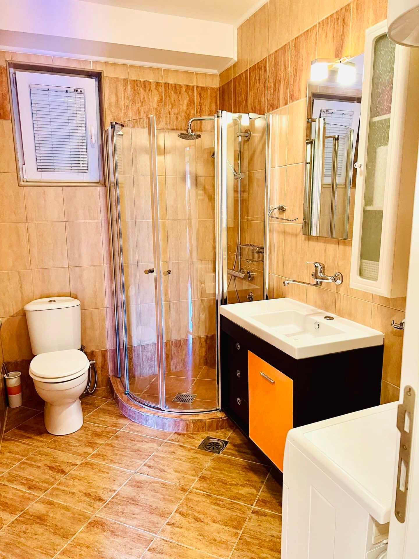 Salle de bains dans un appartement à Petrovac, Monténégro : cabine de douche, meuble vasque et carrelage beige à l’intérieur.