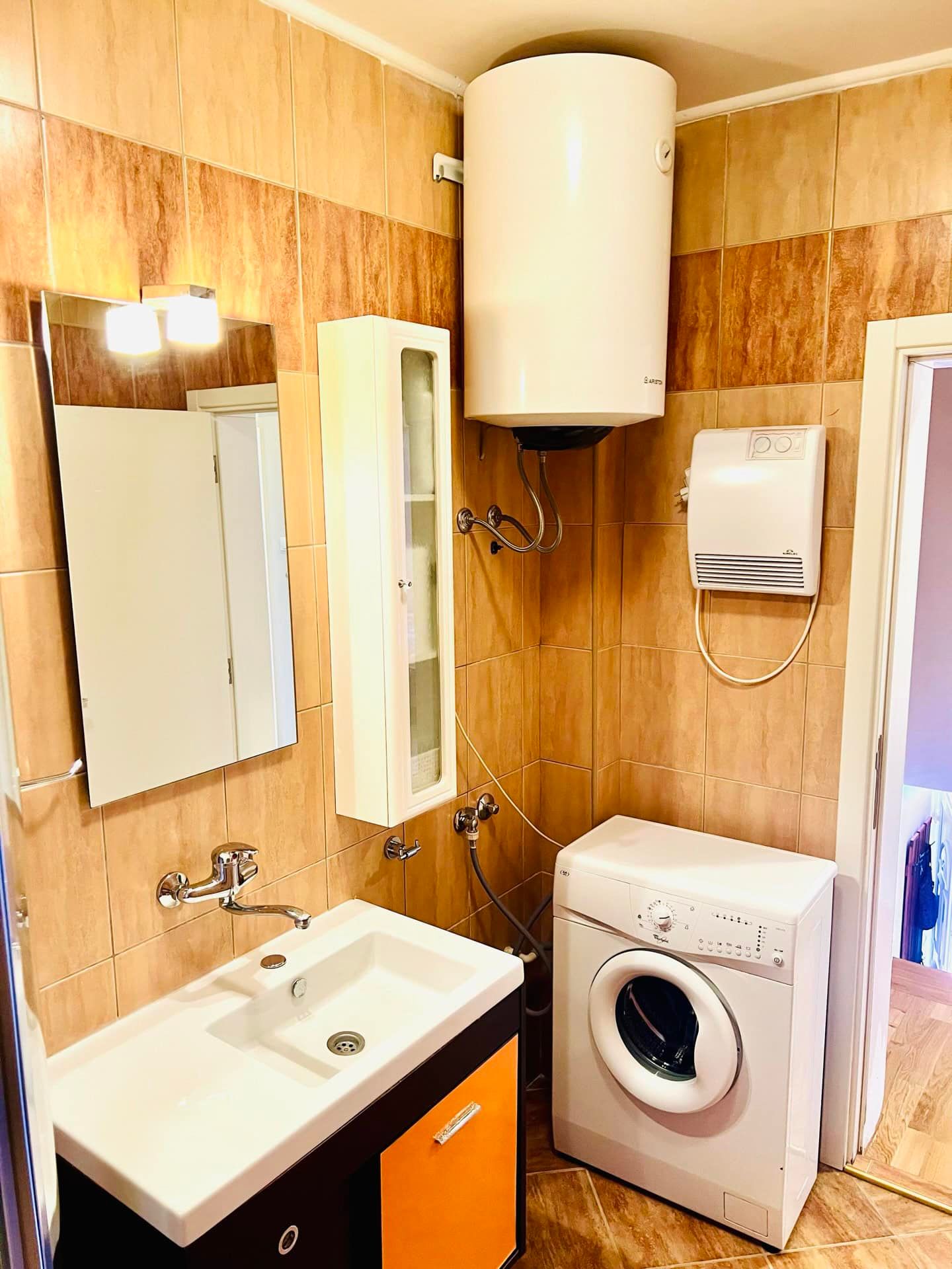 Salle de bain dans un appartement à Petrovac, Monténégro : lavabo avec meuble, miroir, machine à laver et chauffe-eau mural.
