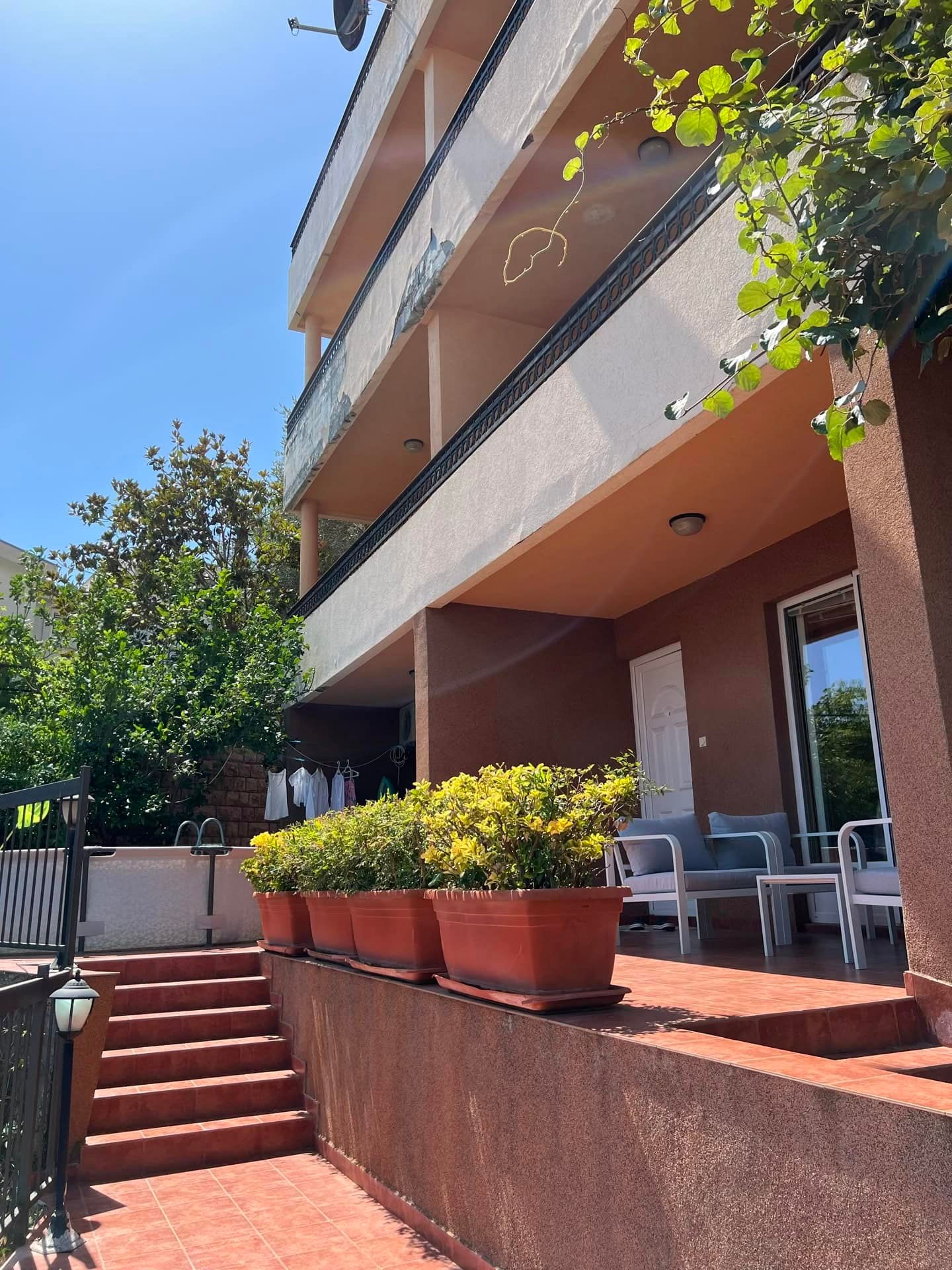 Façade de la maison avec terrasse, mobilier de jardin et plantes à Petrovac, Monténégro. Vue sur les appartements depuis la rue.