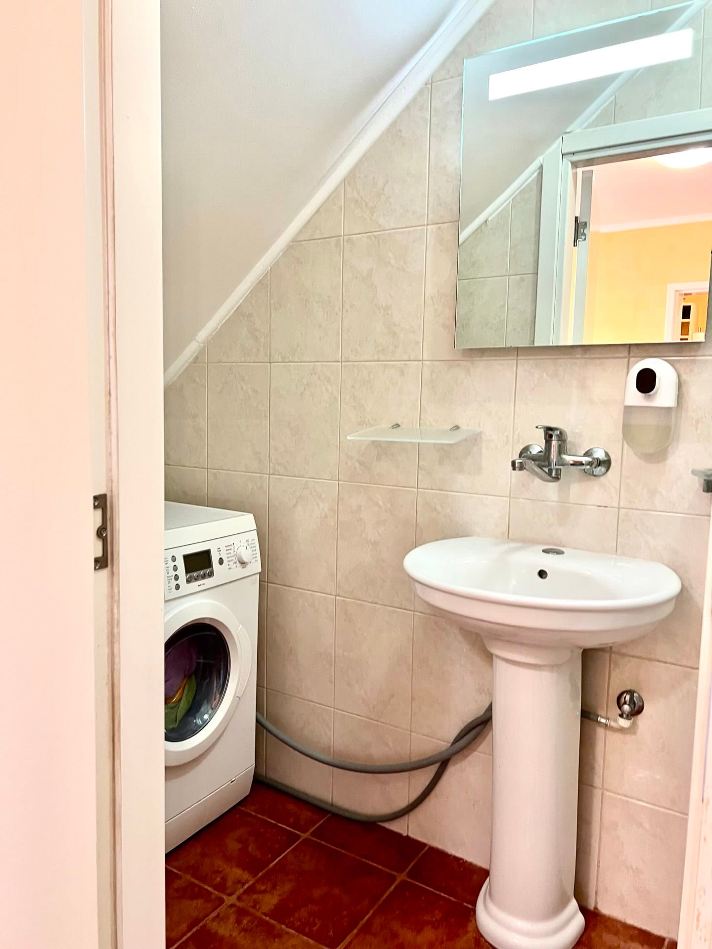 Salle de bains dans un duplex à Petrovac, Monténégro : lavabo sur colonne, miroir et machine à laver sous la pente.