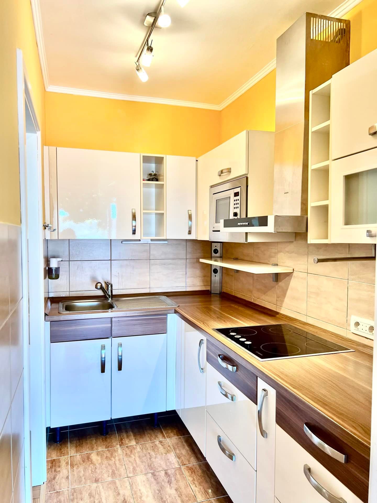 Cuisine moderne dans un appartement à Petrovac, Monténégro : façades blanches brillantes, électroménager intégré et crédence carrelée.